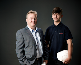 Two people standing; one of them holding a hard-hat